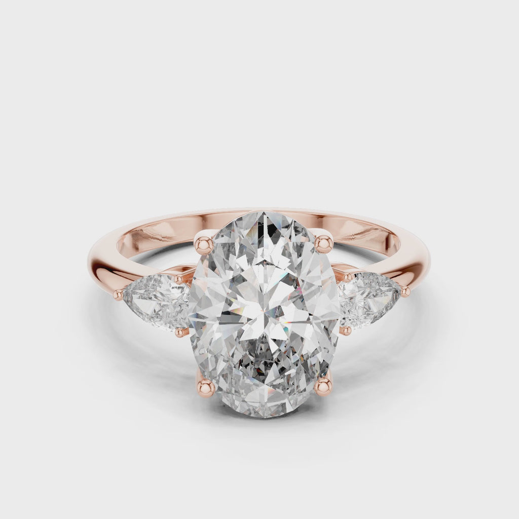 A stunning three-stone lab-grown diamond engagement ring in 14k rose gold, featuring a massive 2.75 carat oval-cut center diamond flanked by two brilliant pear-cut side stones on a clean white background.