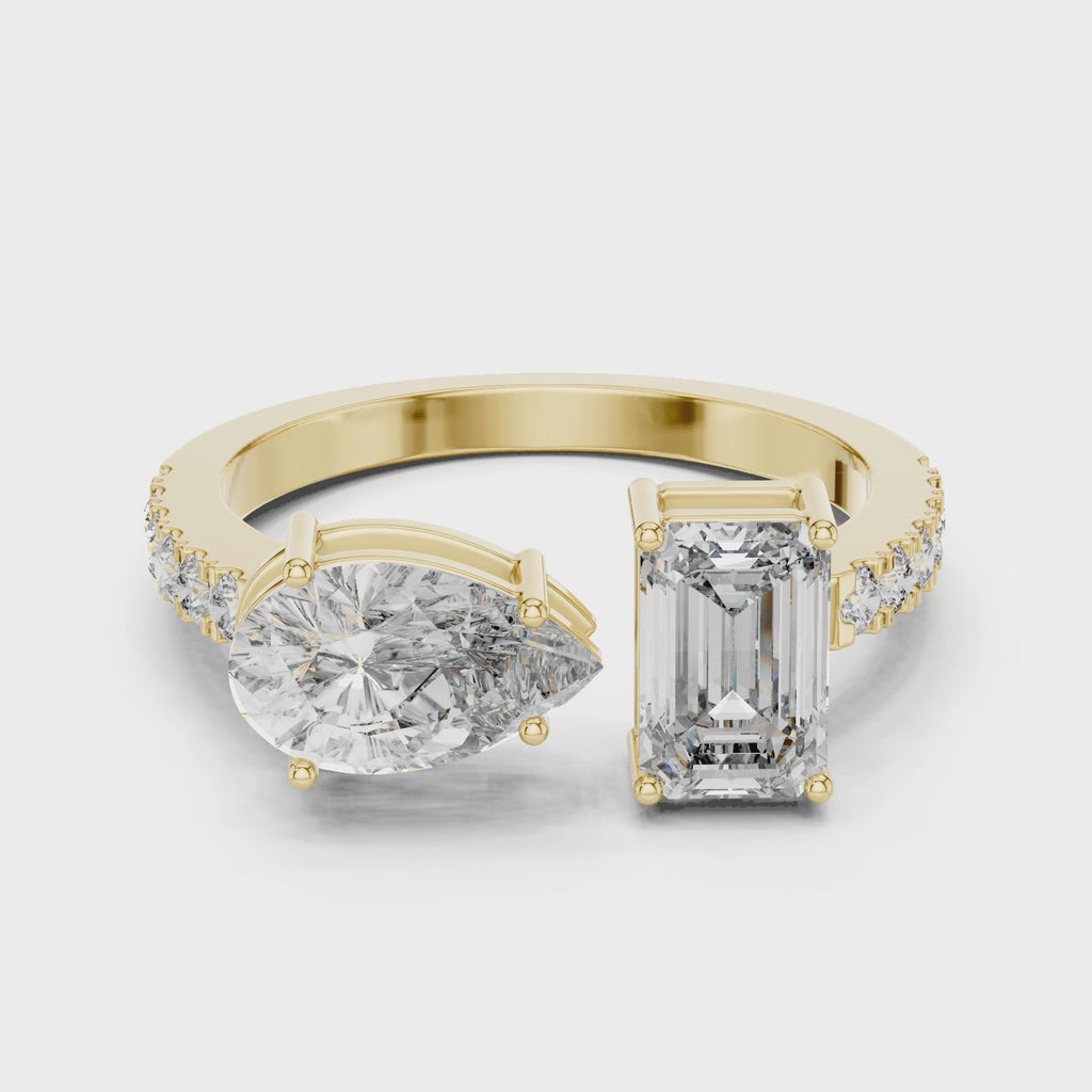 Create alt text for this video showcasing a luxury Toi et Moi engagement ring in solid yellow gold, featuring a 0.86ct emerald-cut diamond paired with a 1.00ct pear-cut diamond on a pavé-accented open band.