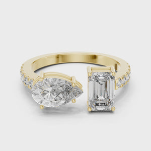 Create alt text for this video showcasing a luxury Toi et Moi engagement ring in solid yellow gold, featuring a 0.86ct emerald-cut diamond paired with a 1.00ct pear-cut diamond on a pavé-accented open band.