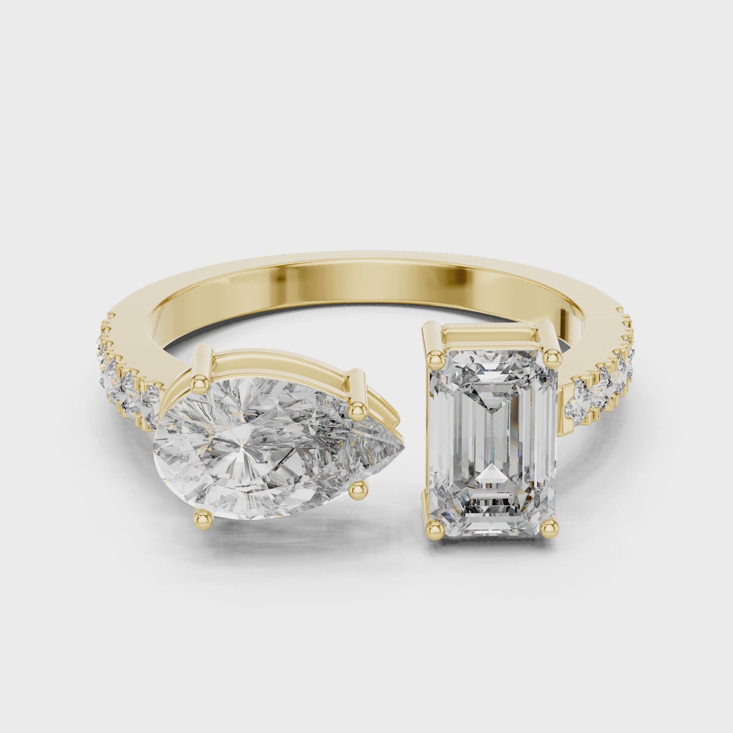 Create alt text for this video showcasing a luxury Toi et Moi engagement ring in solid yellow gold, featuring a 0.86ct emerald-cut diamond paired with a 1.00ct pear-cut diamond on a pavé-accented open band.